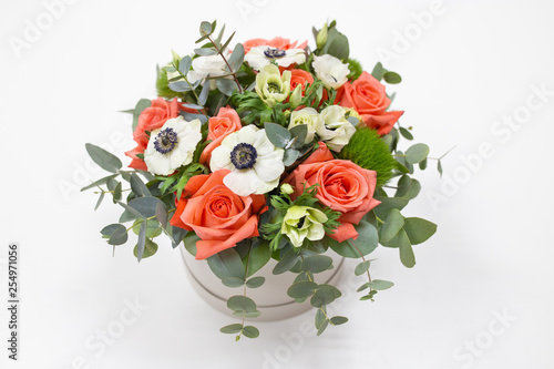 Delicate floral arrangement of roses  anemones  white  pink  orange  and green eucalyptus leaves in a round white cardboard box on a bright background