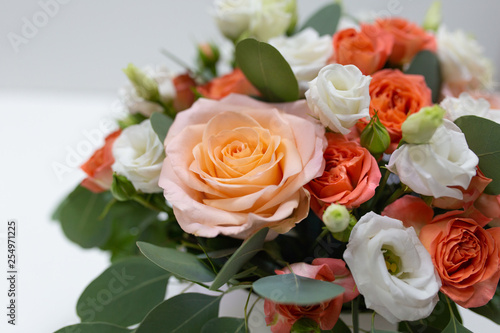 Delicate floral arrangement of roses  white  pink  orange  and green eucalyptus leaves in a round white cardboard box on a light background