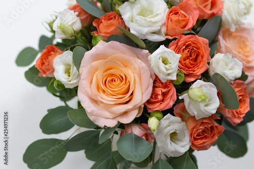 Delicate floral arrangement of roses (white, pink, orange) and green eucalyptus leaves in a round white cardboard box on a light background