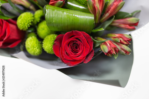 A bright bouquet of fresh flowers  Alstroemeria  Chrysanthemum  Rose  Aspidistra leaves. Primary colors  red and green  in a package made of gray paper in a vase on a light background.