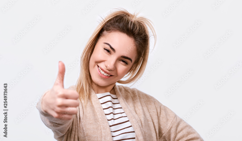 Happy young woman smiling cheerfully and making thumb up sign, showing her support and respect to someone or something. Pretty Caucasian female making positive gesture. Body language. Good job. Happy young woman smiling cheerfully and making thumb up sign, showing her support and respect to someone or something. Pretty Caucasian female making positive gesture. Body language. Good job.