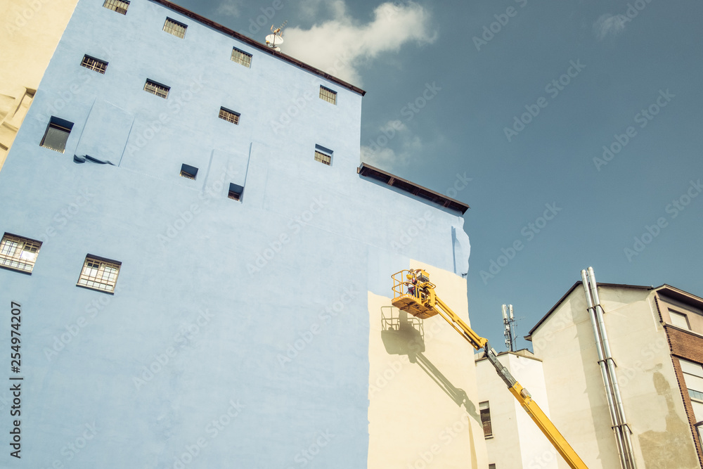 A worker painting the wall of a building. Blue facade of a building A worker painting the wall of a building. Blue facade of a building