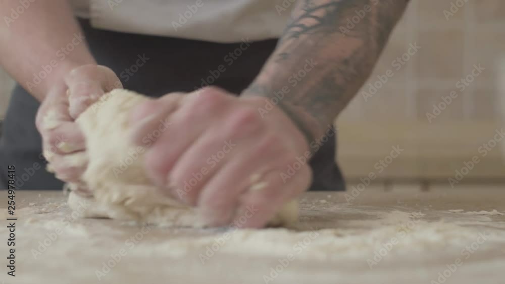 Close up hands of young pizza maker in cook uniform kneading dough for pizza at home in modern kitchen. Concept of food preparation Close up hands of young pizza maker in cook uniform kneading dough for pizza at home in modern kitchen. Concept of food preparation