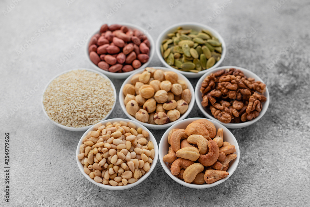 Assortment of nuts in white saucers on a concrete background. Food mix background, top view, copy space, banner