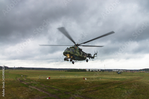 Military helicopter takes off from a grass field in the background of the city