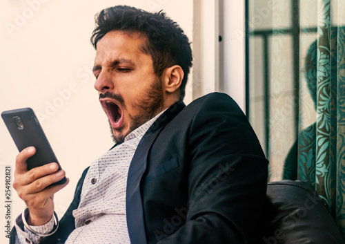 bored man holding smart phone and yawns, front view- image photo