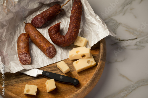 Ringwurst Salami, Bierbeißer Wurst und Edamer Käse in Wachspapier mit Messer auf Vesper Holzbrett photo