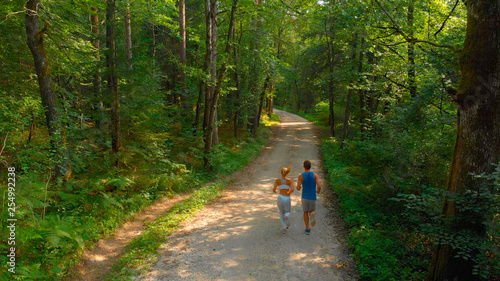 DRONE: Athletic couple jogging down gravel trail running through the woods.