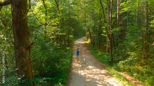 AERIAL: Flying behind unrecognizable fit couple jogging down the forest trail.