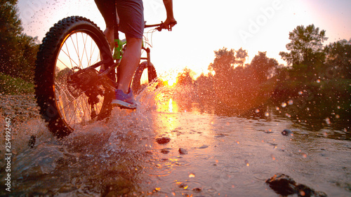 LENS FLARE: Sportsman riding his bicycle in the shallow stream towards sunset. photo