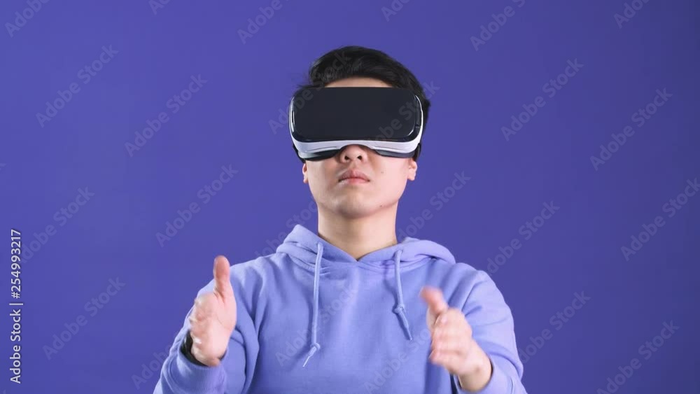 Asian young man using virtual reality headset isolated over violet background. Asian young man using virtual reality headset isolated over violet background.