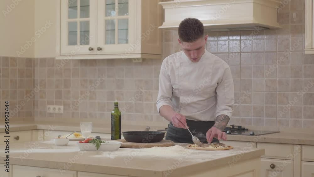 Pizza maker prepares pizza in the kitchen. Man putting freshly roasted meat from skillet on pizza base. Concept of food preparation. Pizza maker prepares pizza in the kitchen. Man putting freshly roasted meat from skillet on pizza base. Concept of food preparation.