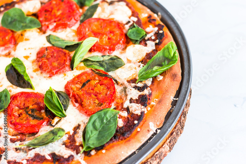 Margherita Pizza - a Thin crust Pizza Topped with Tomatoes, Fresh Mozzarella, and Fresh Basil Leaves. Extreme Close-Up of Margherita Flat Bread Pizza on Gray / White Textured Background..