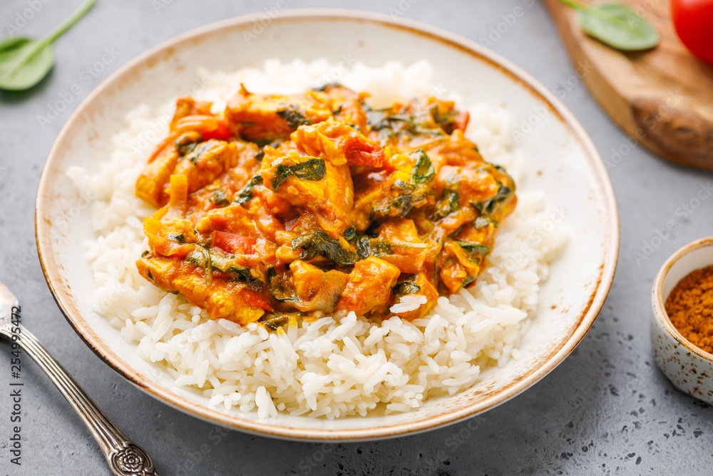White rice with Bombay chicken curry with spinach, tomato and onion in a white frying pan on a kitchen table. Indian traditional cuisine. White rice with Bombay chicken curry with spinach, tomato and onion in a white frying pan on a kitchen table. Indian traditional cuisine.