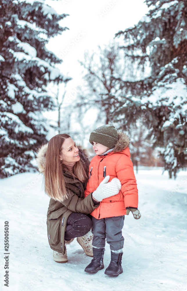 A young mother talks to her son, a little boy of 3-5 years old. Winter in the woods in the fresh air. Emotions of joy fun, rest on weekends snow drifts green Christmas trees background.