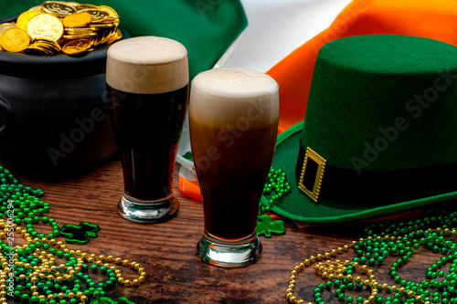 St Patricks day party and Irish celebration of patron saint concept theme with frothy glasses of dry stout, green hat with a buckle, a pot of gold, the flag of Ireland and beads with shamrock in a pub photo