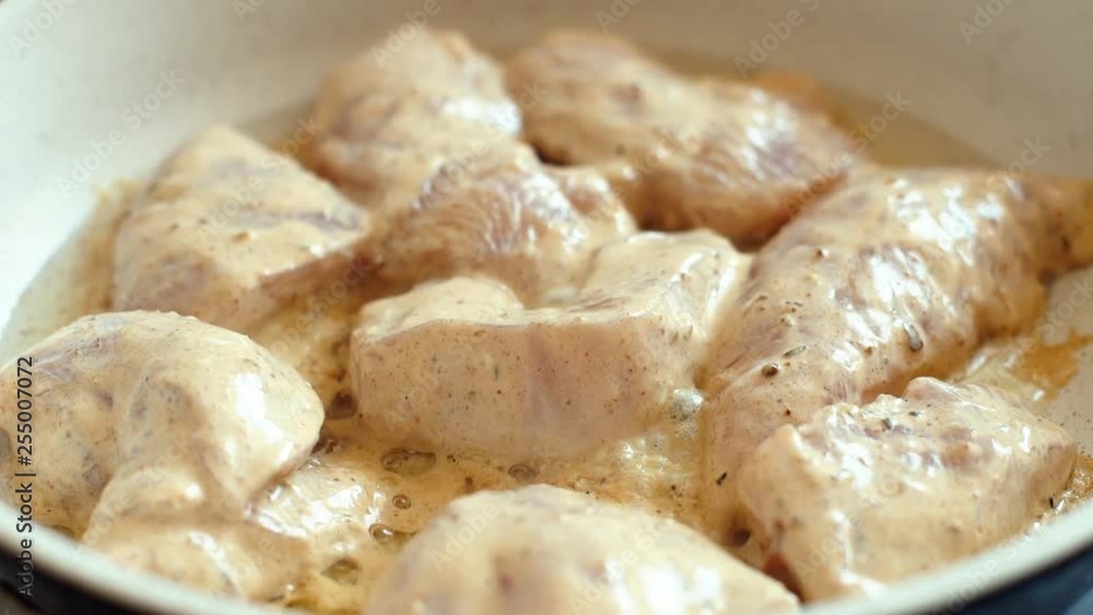 Chicken meat in cream sauce is frying in pan. Close up shot, frying oil demonstration