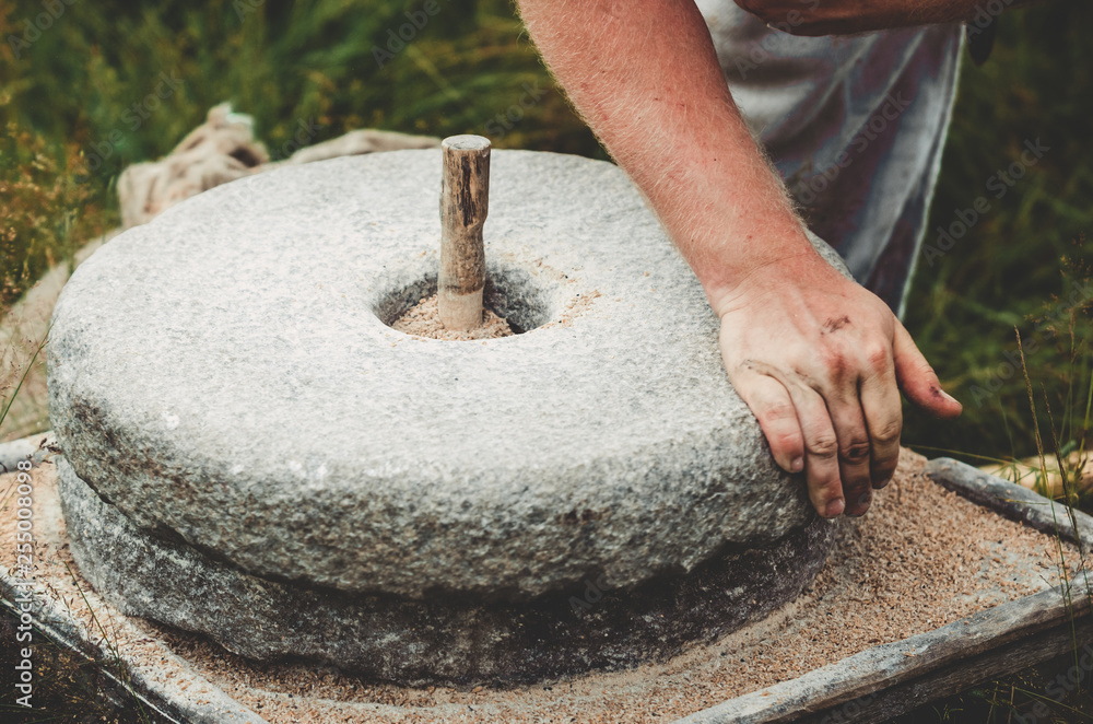 The ancient quern stone hand mill with grain. The man grinds the grain