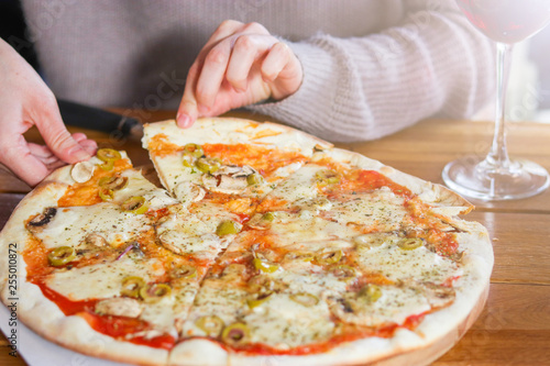 woman  takes a slice of sliced Pizza with Mozzarella cheese, Tomatoes, pepper, olive, Spices and Fresh Basil. Italian pizza. Pizza Margherita or Margarita on wooden table background
