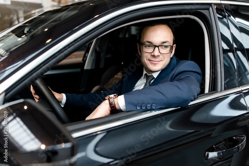 Businessman sitting behind the wheel of a black car outside view © pantovich