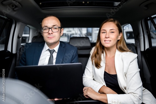 Business partners man and woman sitting in the car working on a laptop