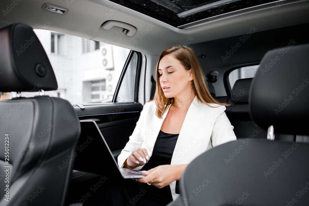 Business lady sitting in the car working on a laptop