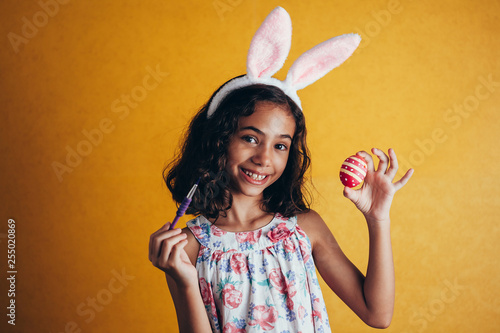 A happy girl painting Easter eggs over color background