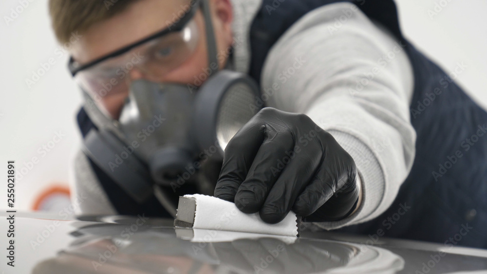 A professional male (boy) master of ceramics of a car puts ceramics on a car using a fiber (sponge) rag in a puller, safety goggles and black gloves. A professional male (boy) master of ceramics of a car puts ceramics on a car using a fiber (sponge) rag in a puller, safety goggles and black gloves.