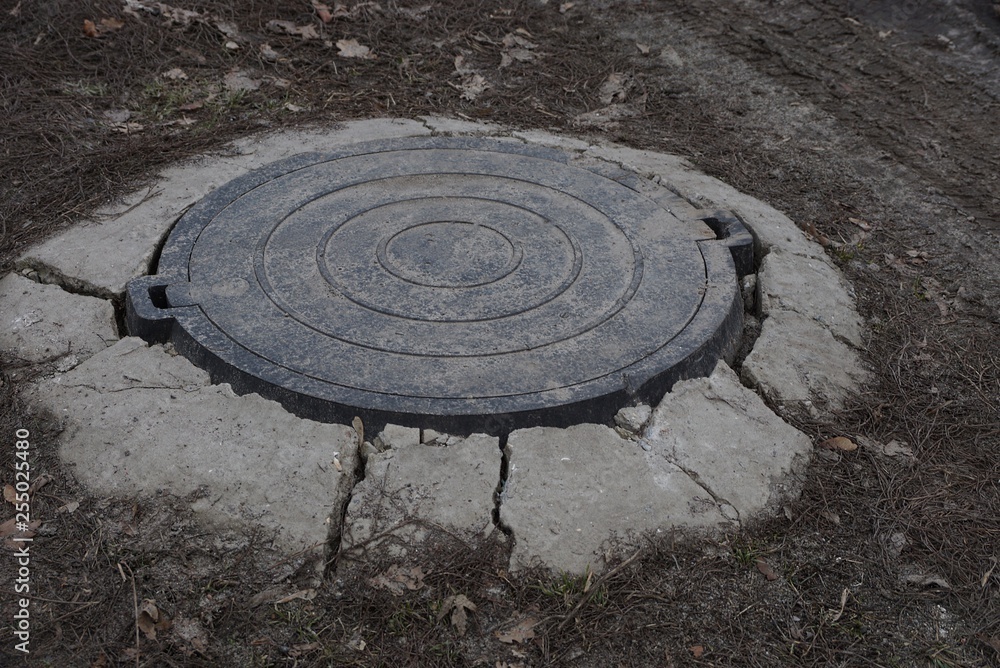 one gray round iron manhole lays on the road in concrete and dry grass
