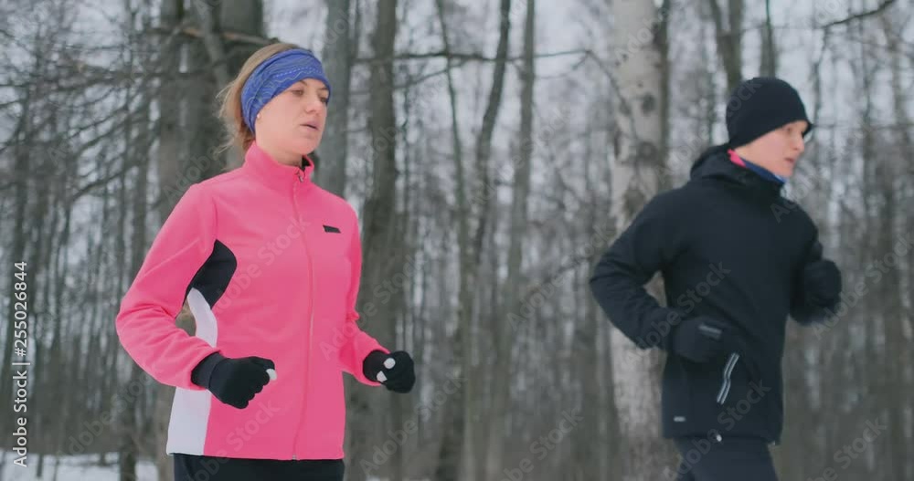 Young man and woman on a morning run in the winter forest. A woman in a loose jacket a man in a black jacket is running through a winter park. Healthy lifestyle happy family. Young man and woman on a morning run in the winter forest. A woman in a loose jacket a man in a black jacket is running through a winter park. Healthy lifestyle happy family.
