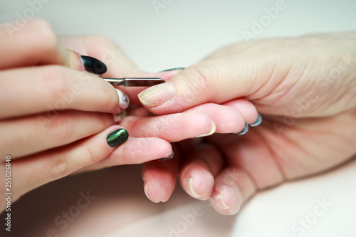 nail service manicurist makes an elderly woman manicure with a metal tool - a lancet with a spatula at the end. Moving off the nail cuticle. reporting shooting.