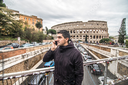 Photography Young man talk on mobile phone on the street in Rome with colosseum on backgroun