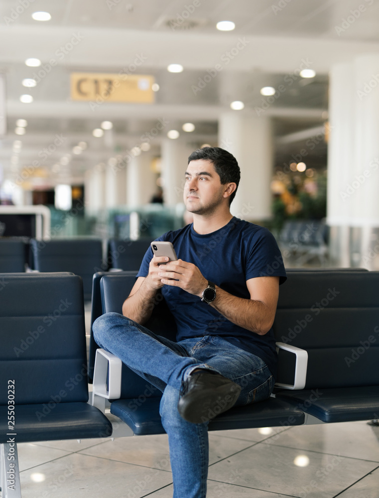 Texting he is fine. Portrait of handsome smiling man in casual wear holding his luggage and messaging through his mobile phone while sitting in the hall of the airport Texting he is fine. Portrait of handsome smiling man in casual wear holding his luggage and messaging through his mobile phone while sitting in the hall of the airport