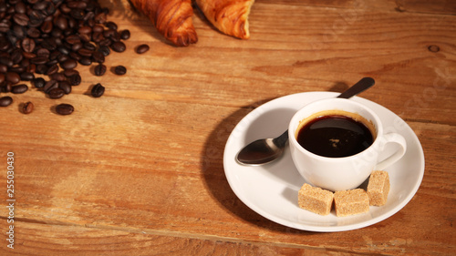 Coffee white cup, croissants on wooden table and roasted coffee beans. Breakfast concept