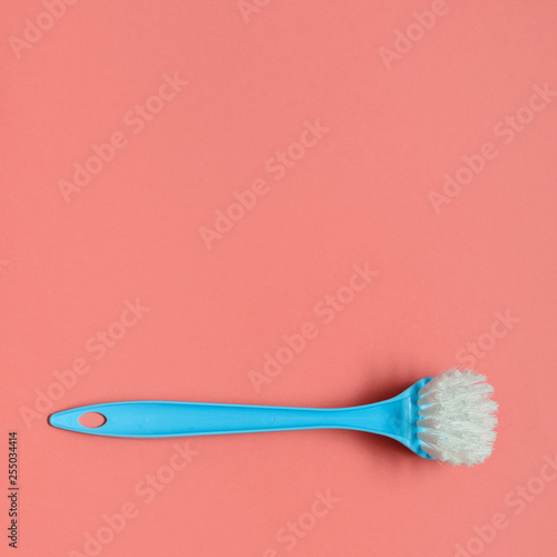 Pale blue brush for washing dishes lying on living coral background. In the style of pop art. Top view. Copy space.