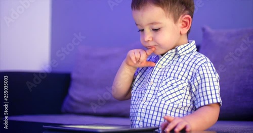 Cute Child Entertaining With Tablet. Little Boy Spending Leisure Time Playing Mobile Game in the and Crushes the Bright Screen With Her Hand. Concept of:Happy Childfood, Technology, Childen Play Games photo