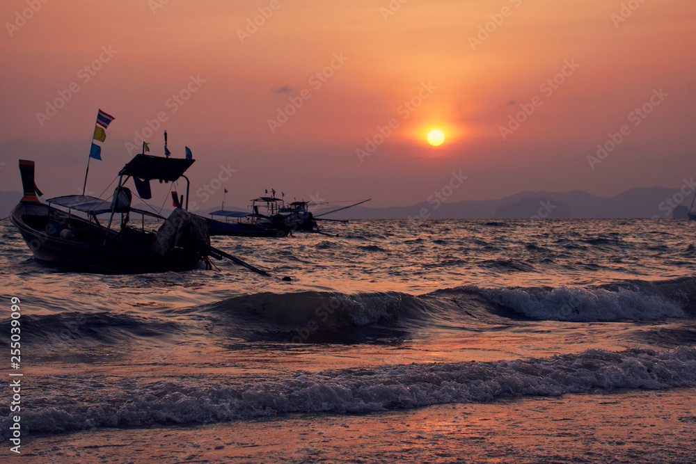 Long-tailed boat in wavy sea during sunset at Khlong Muang Beach, Krabi, Thailand.