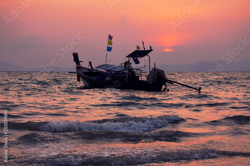 Long-tailed boat in wavy sea during sunset at Khlong Muang Beach, Krabi, Thailand. photo