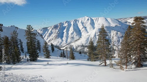 A pan of the snow covered high Sierras with a rugged mountainous peak in the background under a bright blue sky in February