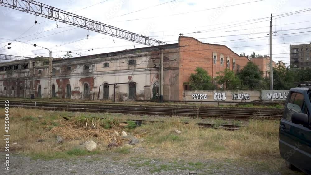 Green old locomotive pass in front of old crumbling buildings in Tbilisi Georgia, graffiti wall in the background