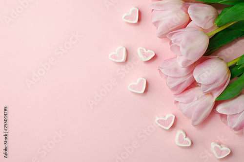 Fototapeta Naklejka Na Ścianę i Meble -  Pastel pink tulip flowers bouquet and heart shaped candy on pink background. Flat lay, top view. Minimal floral springtime flatlay concept