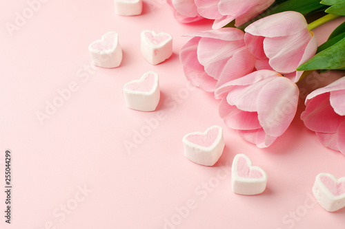 Pastel pink tulip flowers bouquet and heart shaped candy on pink background. Flat lay  top view. Minimal floral springtime flatlay concept