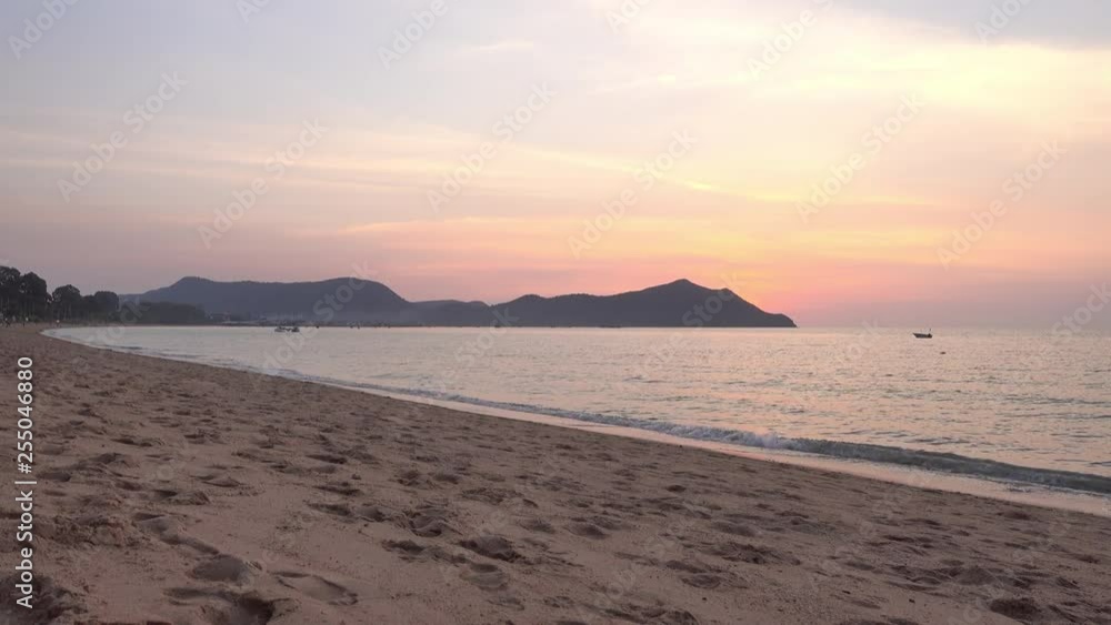 magic hour sunset on empty clean sand beach with calm ocean and red golden blue gradient of dawn on a clear sunny day, locked shot, no people, mountain shoreline on the horizon