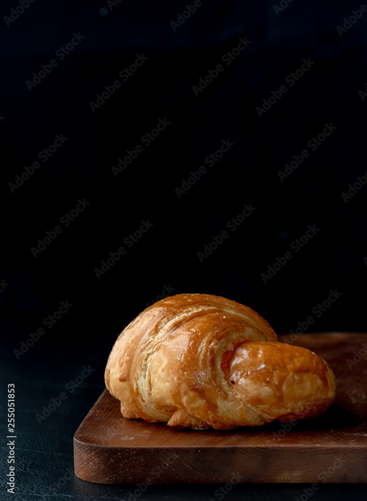 Croissant with icing on wood board in Chiaroscuro photo style, black background. Croissant with icing on wood board in Chiaroscuro photo style, black background.