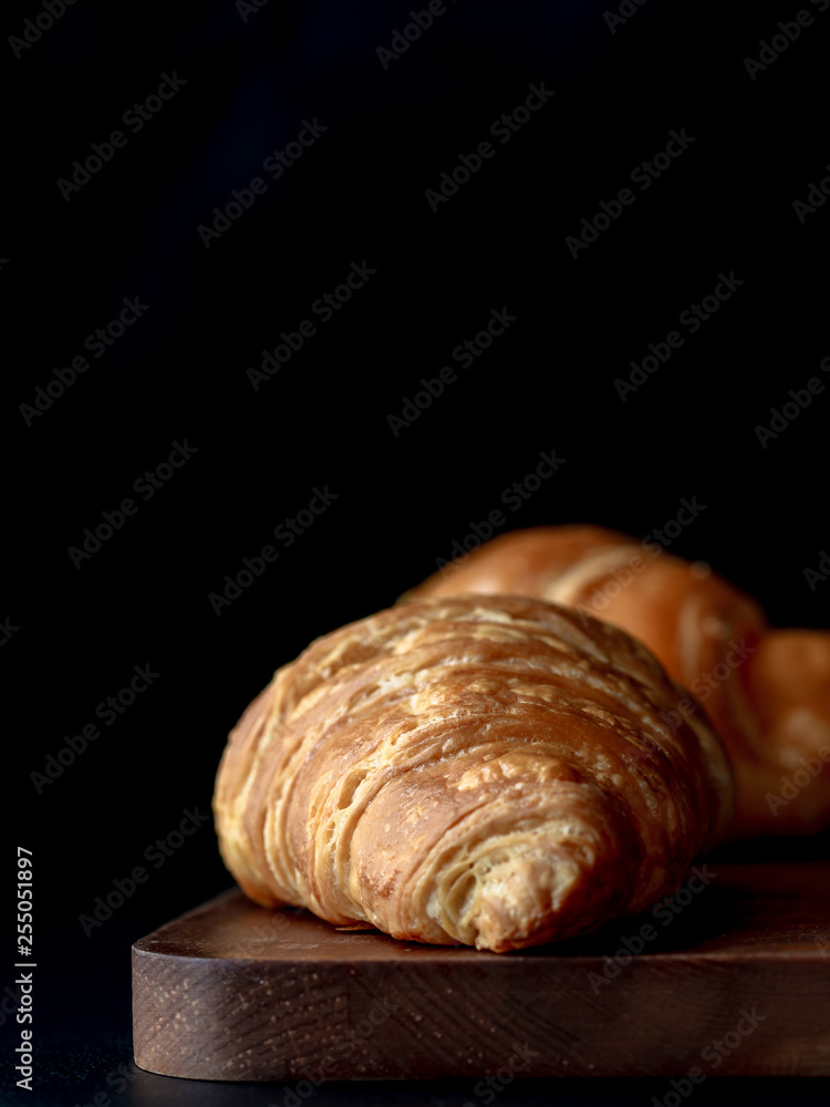 Croissant with icing on wood board in Chiaroscuro photo style, black background. Croissant with icing on wood board in Chiaroscuro photo style, black background.