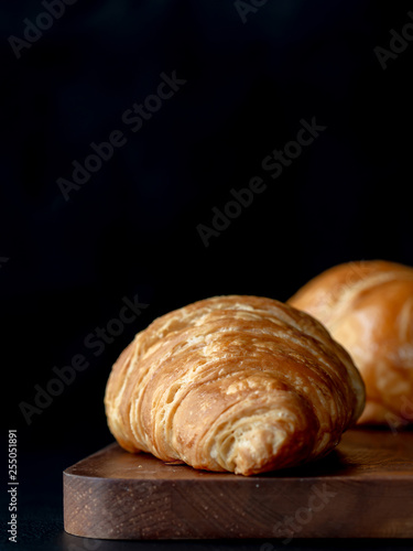 Croissant with icing on wood board in Chiaroscuro photo style, black background.