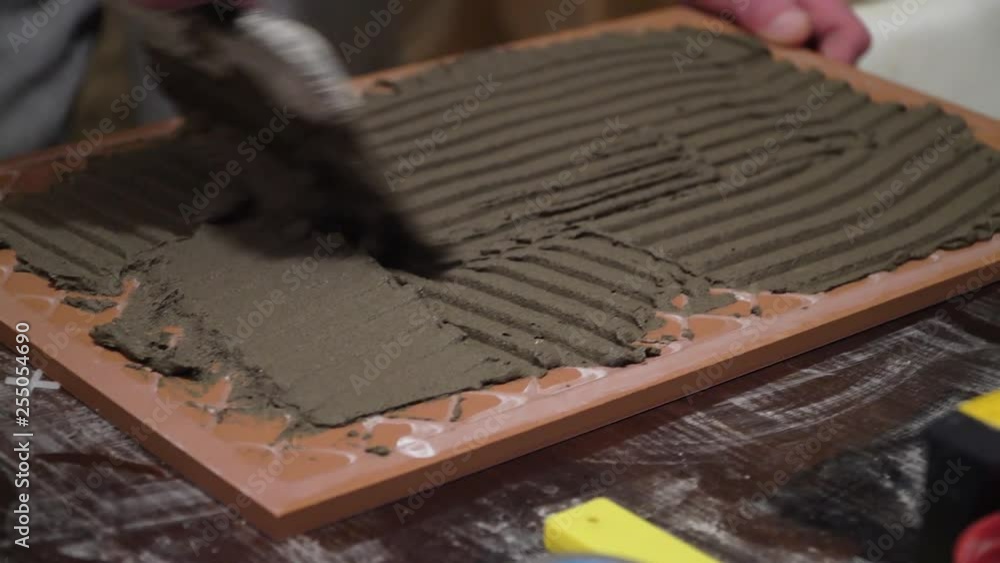 Worker applies cement adhesive on the tiles. Finishing works, focus on hands. The technology of laying tile.