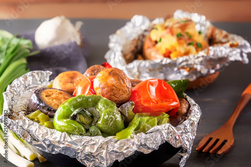 Baked vegetables in foil - tomatoes, eggplants, peppers and baked potatoes with bacon, onions on a gray wooden table. Close-up