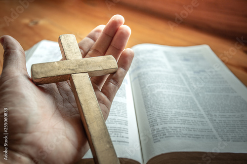 Christian holding wooden cross in hands on bible. religion concept.