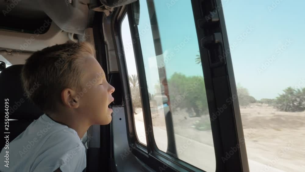Boy enjoying cool wind blowing to his face when he traveling by car and looking out the open window Boy enjoying cool wind blowing to his face when he traveling by car and looking out the open window